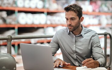 Mann arbeitet konzentriert am Laptop in moderner Umgebung – Weiterbildung zu Warenursprung, Präferenzen und Lieferantenerklärungen im Außenhandel.