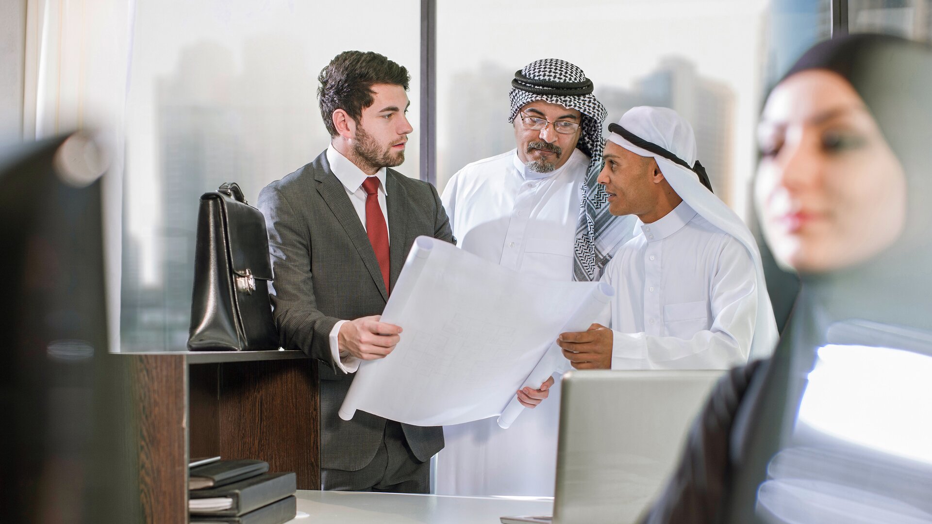 Geschäftsmeeting zwischen internationalem Team mit Bauplänen im modernen Büro