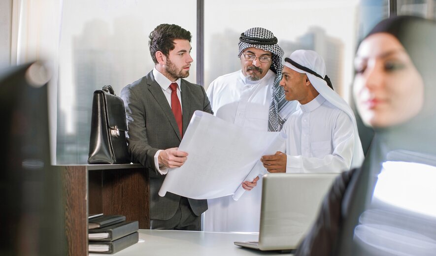 Geschäftsmeeting zwischen internationalem Team mit Bauplänen im modernen Büro