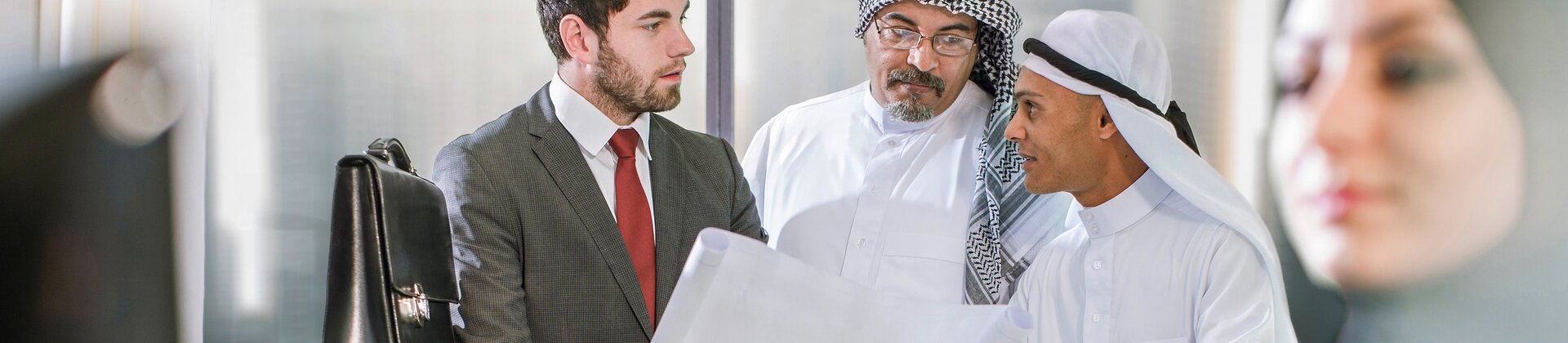 Geschäftsmeeting zwischen internationalem Team mit Bauplänen im modernen Büro
