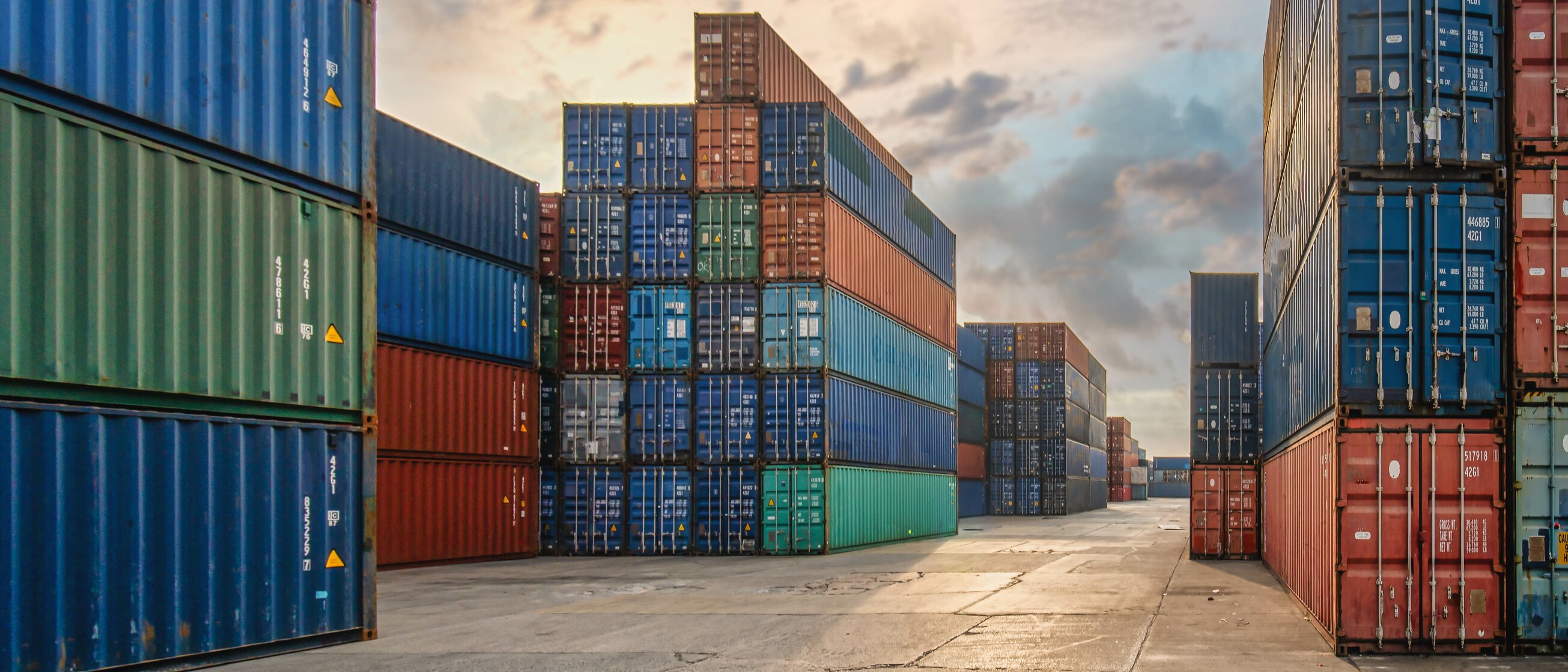 Gestapelte bunte Schiffscontainer im Hafen bei Sonnenuntergang – Symbol für internationalen Warenverkehr, Import, Export und Zollabwicklung.