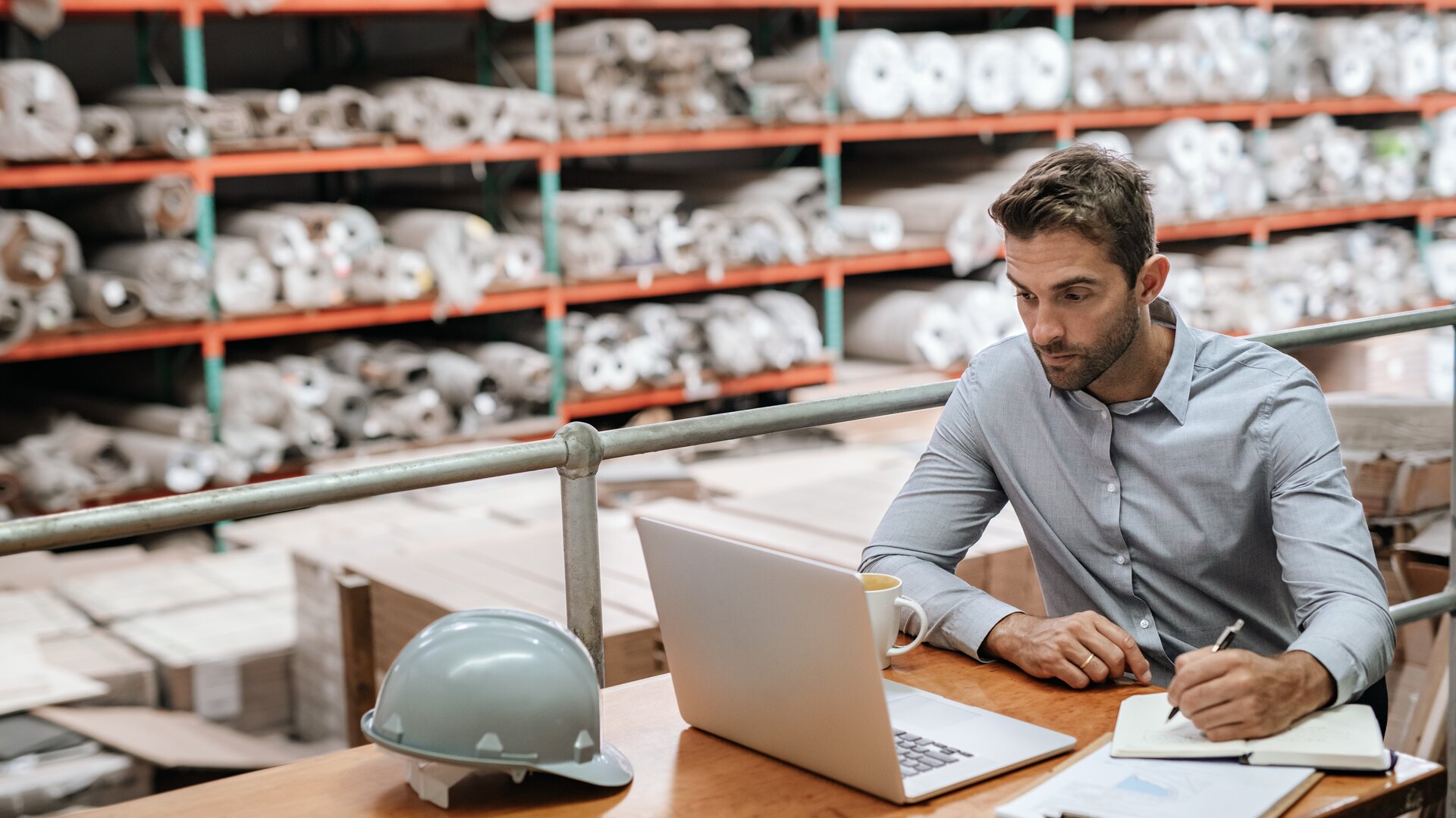 Weiterbildung Gepr. Fachwirt/-in für Einkauf: Mann arbeitet im Lager mit Laptop und Unterlagen an Einkaufs- und Beschaffungsaufgaben.