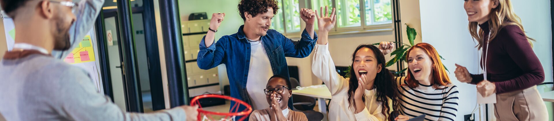E-Sport und Gaming im HR: motiviertes Team im Büro feiert Erfolg bei spielerischer Teambuilding-Aktivität mit Mini-Basketball und digitaler Zusammenarbeit