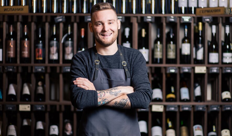 Weiterbildung Junior Sommelier/-ière IHK: Sommelier steht vor Weinregalen und präsentiert seine Fachkompetenz.