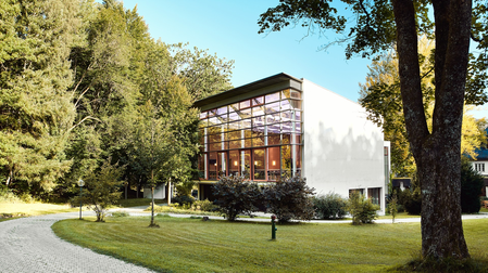 Außenansicht eines Großen Saals mit heller Glasfront umgeben von Bäumen in Feldkirchen-Westerham