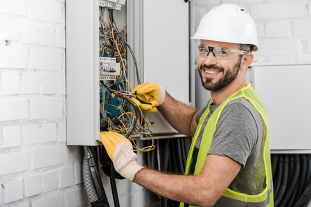 Elektrofachkraft mit Schutzhelm arbeitet an Schaltschrank – Symbol für Sicherheitsunterweisung im Elektrobereich.