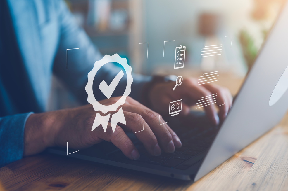 Hand arbeitet am Laptop mit digital eingeblendetem Qualitätssiegel – symbolisiert die zertifizierte Qualität, Professionalität und Praxisnähe der IHK Akademie München und Oberbayern.