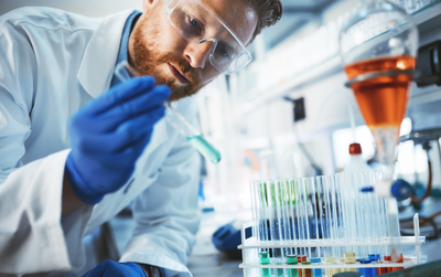 Chemiker arbeitet im Labor mit Reagenzglas und Schutzbrille – Sinnbild für fundiertes Fachwissen und technische Kompetenz in der Weiterbildung zum/zur Geprüften Industriemeister/-in Chemie.