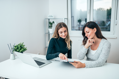 Zwei Frauen besprechen Lernunterlagen am Schreibtisch – Sinnbild für Weiterbildung, Aufstieg und Abschluss auf Bachelor-Niveau in der Veranstaltungstechnik.