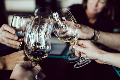 Personen stoßen mit Weingläsern an beim Abendessen in der Akademie Westerham mit regionalen Weinen und Getränken