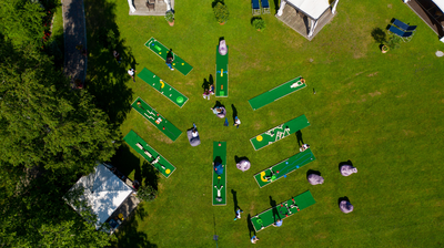 Luftaufnahme einer Minigolfanlage beim Westerhamer Teamevent: Mehrere bunte Bahnen sind auf einer Wiese aufgebaut, Teilnehmende spielen und messen sich beim Selfmade-Minigolf-Turnier