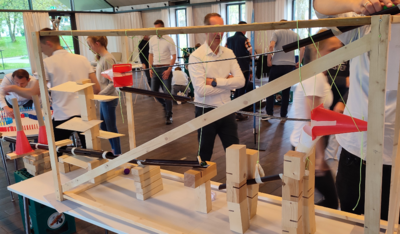 Teilnehmende bauen gemeinsam eine Kettenreaktion mit Holzbausteinen und Kugeln