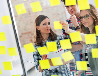 Frau arbeitet an Whiteboard mit Haftnotizen, um mentale Stärke und Resilienz für Prüfungsphasen zu trainieren.