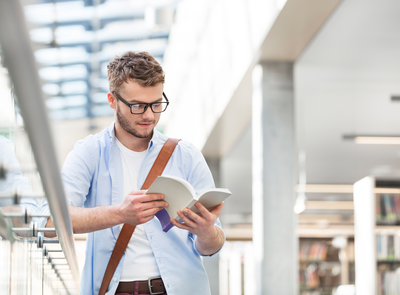 Student liest konzentriert in der Bibliothek und bereitet sich strukturiert auf Prüfungen vor.