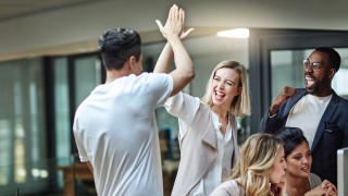 Shot of a group of colleagues giving each other a high five while using a computer together at work