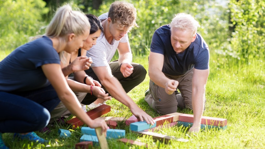 Serious male and female friends planning while stacking building blocks on grassy field in forest