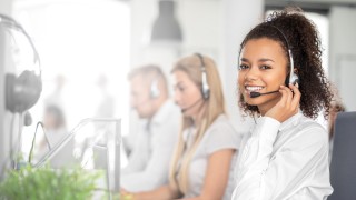 Call center worker accompanied by her team. Smiling customer support operator at work. Young employee working with a headset.