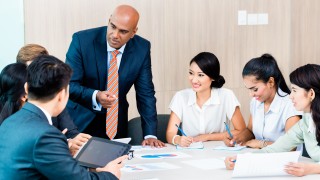 Diversity team in business development meeting with charts, Indian CEO and Caucasian executive crunching numbers, charts and figures on the desk