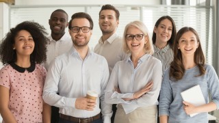 Smiling multiethnic employees standing looking at camera making team picture in office together, happy diverse work group or department laugh posing for photo at workplace, show unity and cooperation
