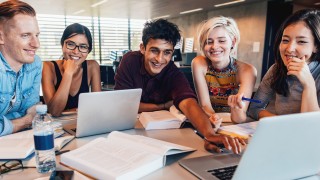 Multiethnic group of young people studying together at a table looking at laptop. Young students in cooperation with their school assignment.