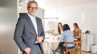 Confident businessman in office with employees in background
