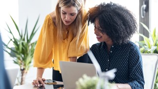 Shot of business women working together with laptop an a digital tablet while talking in modern workspace.