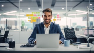 Busy Young Businessman Using Laptop Computer in Modern Office. Manager Thinks About Successful Financial Ideas. Happy Man Smiling About Finding Problem Solving Solutions for Company.