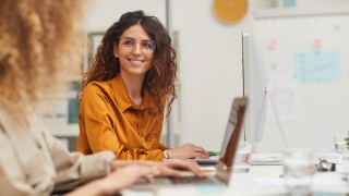 Two beautiful female colleagues interacting while working in office