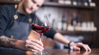 Skilled sommelier pouring wine. Man in black suit and white shirt looks concentrated: he's evaluating quality of wine being pouring. Process of tasting wine captured in photo.