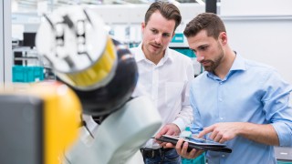 Two men with tablet examining assembly robot in factory shop floor