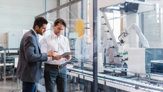 Two businessmen with tablet talking in modern factory