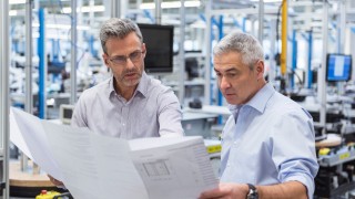 Two businessmen in factory hall discussing construction plan