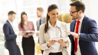 Young business couple is working on a tablet while other young business people talking in the background