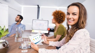 Smiling businesswoman using digital tablet while colleagues discussing in meeting at creative office