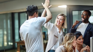 Shot of a group of colleagues giving each other a high five while using a computer together at work