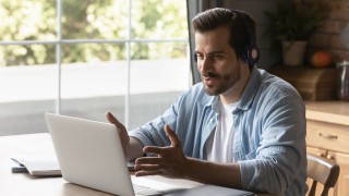 Young Caucasian man wear headphones look at laptop screen talk speak on video call online. Millennial male in earphones use computer have webcam digital virtual conference. Technology concept.